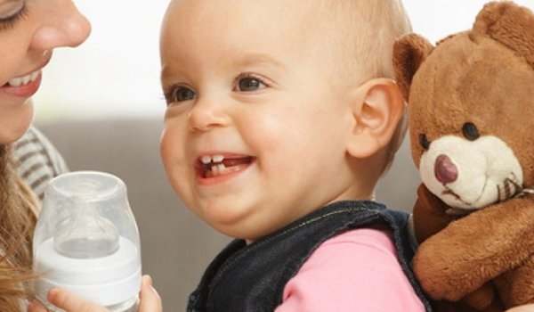 Lachendes Baby hält Babyflasche in der Hand