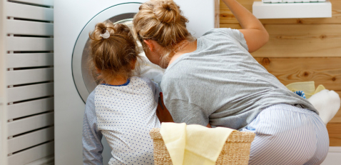 Mutter und Tochter schauen zu wie die Waschmaschine wäscht.