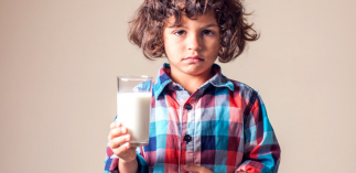 Kind mit einem Glas Milch in der Hand greift sich auf dem Bauch und hat einen schmerzverzerrten Ausdruck im Gesicht.   
