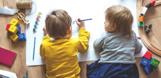 Zwei Kleinkinder liegen am Boden und Zeichnen etwas auf einen Malblock. 
